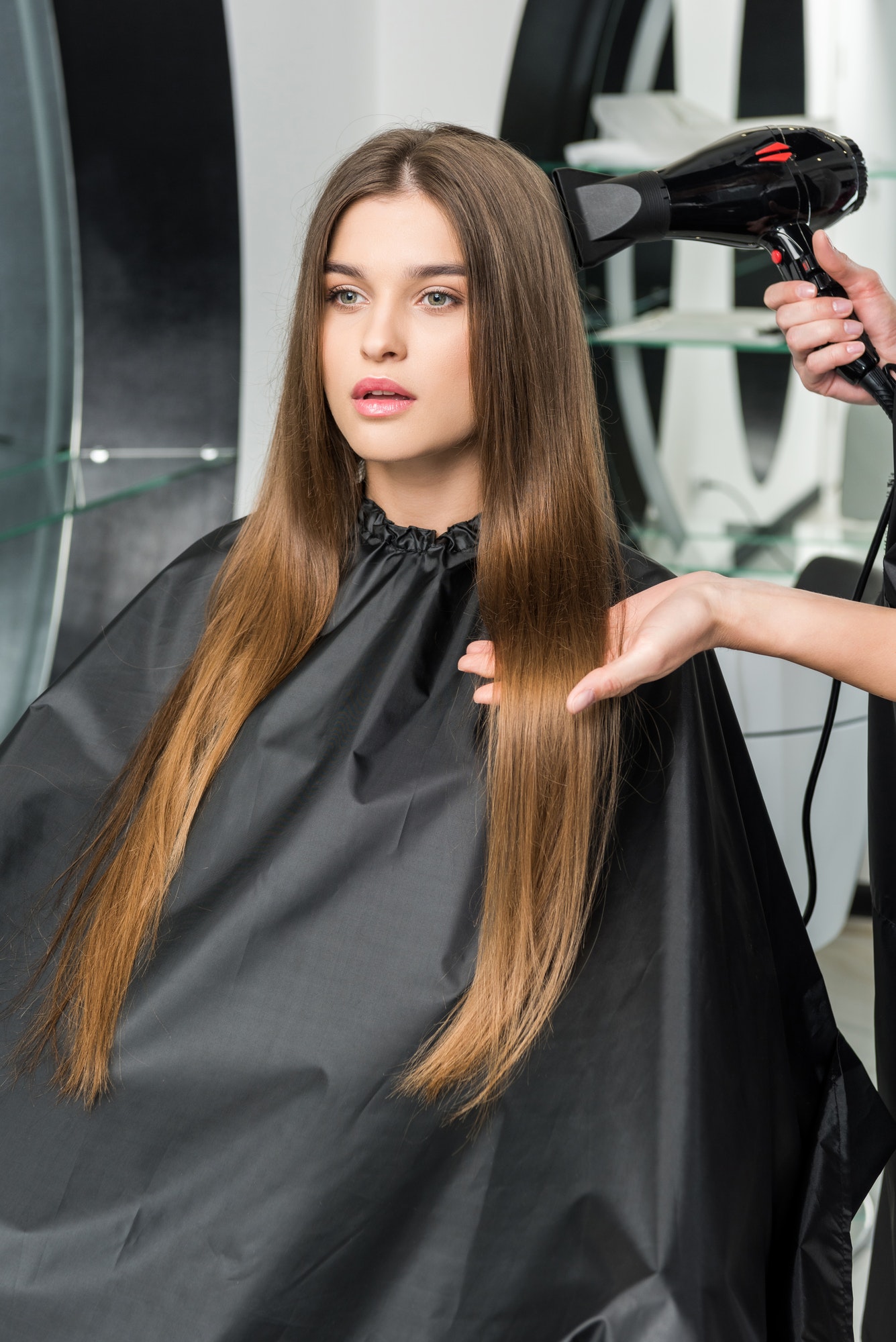 hairdresser drying long hair of young woman in beauty salon