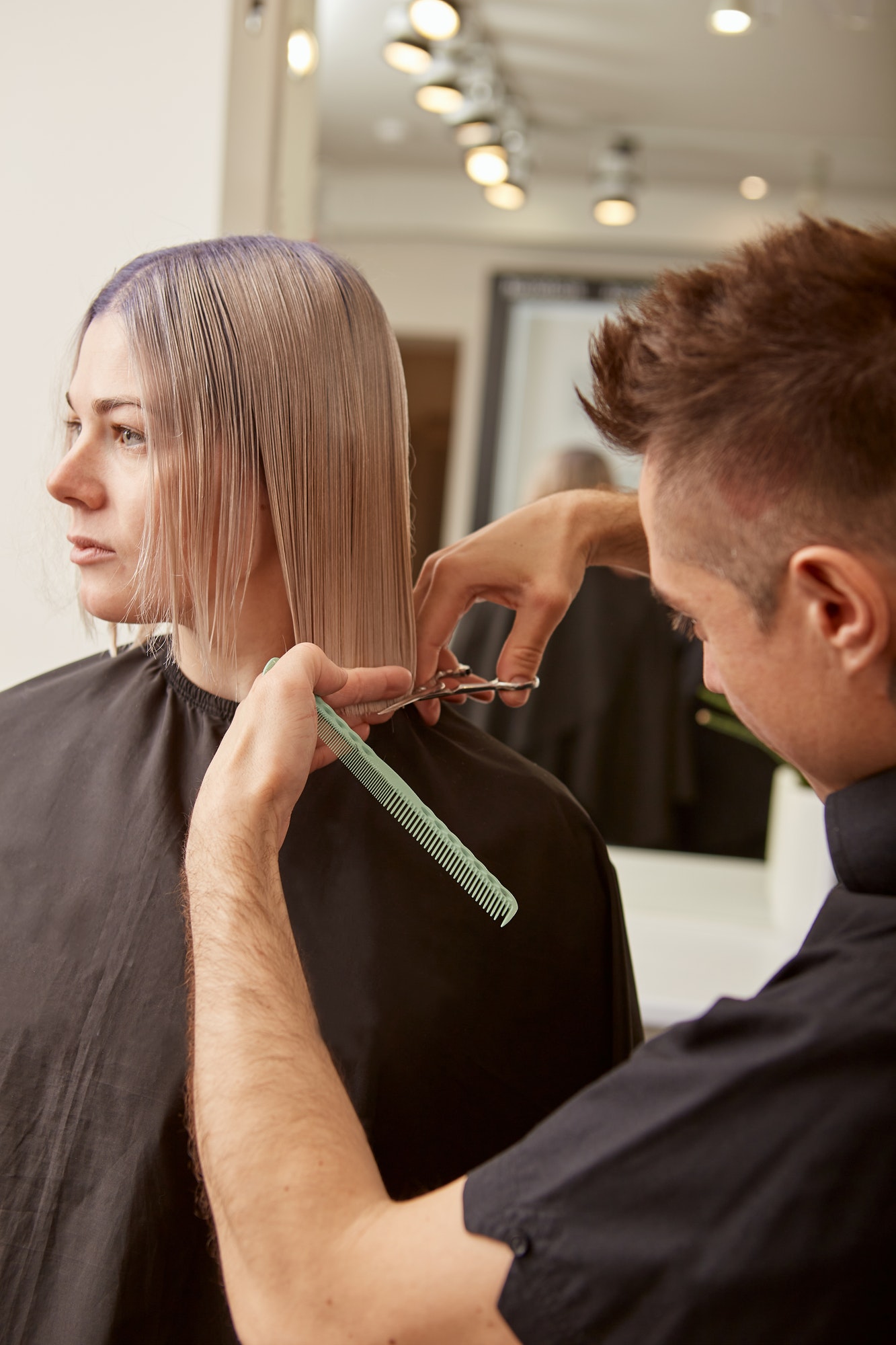 Male hairdresser cutting woman hair in beauty salon